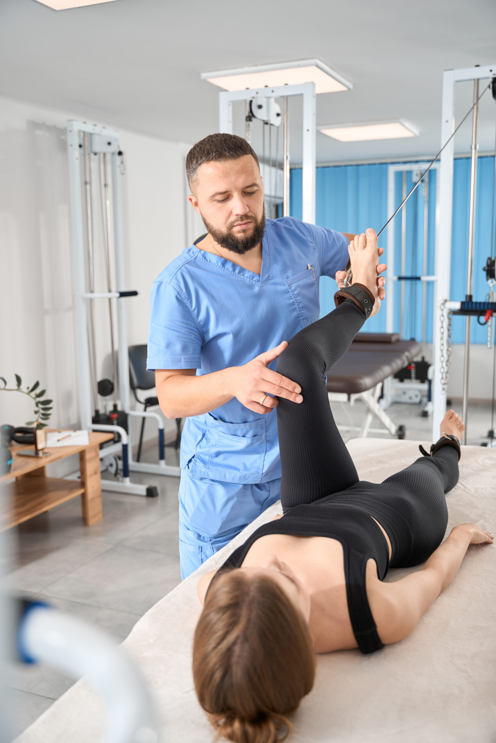 Physiotherapist uses a special exercise machine to work with a patient, a woman lies on a massage table